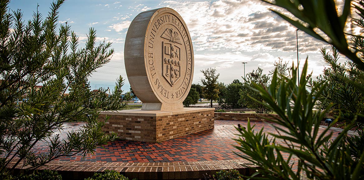 ttuhsc seal behind some trees on a brick circle