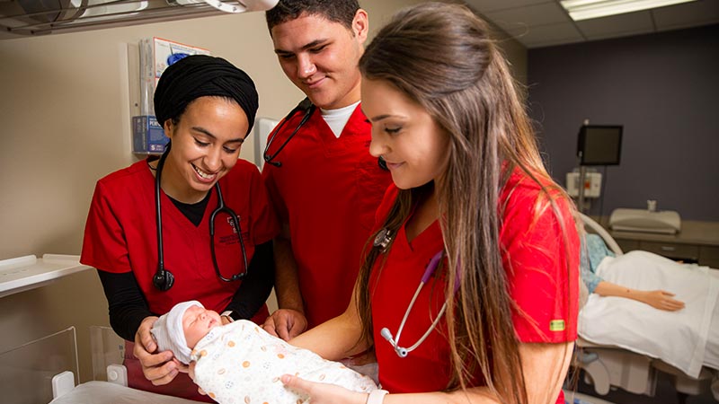 three nursing students holding and staring at a baby doll