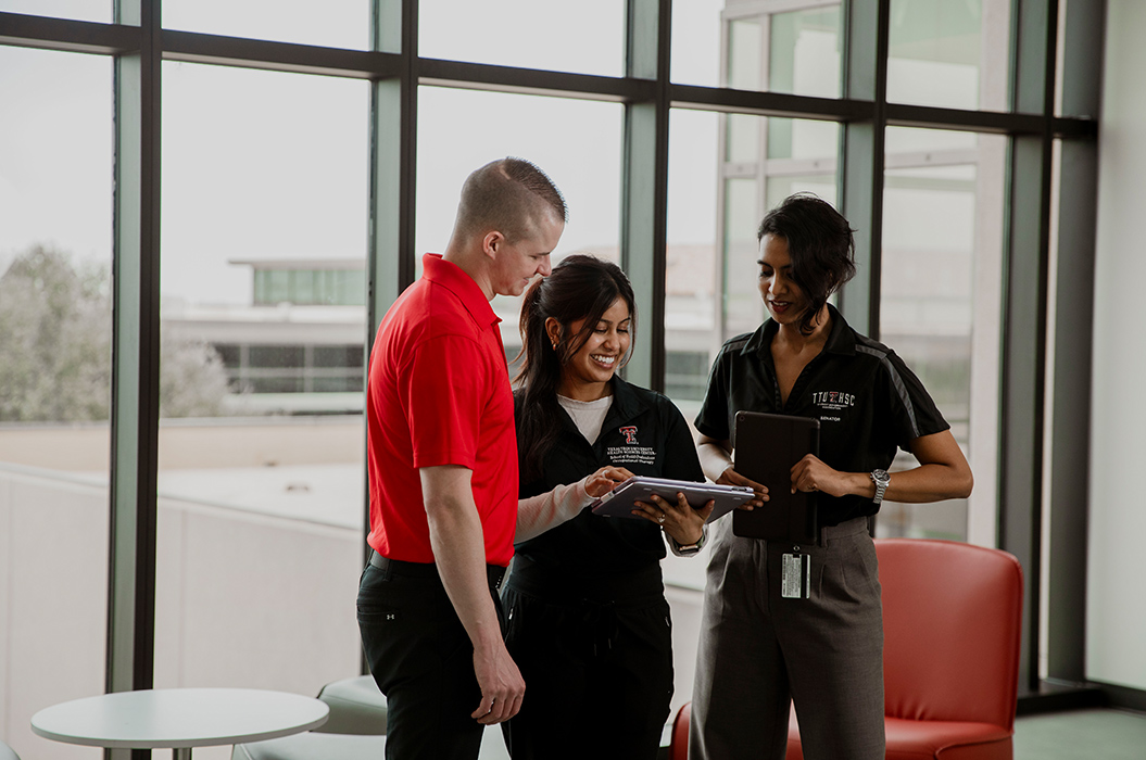 three health professions students standing smiling looking at a tablet