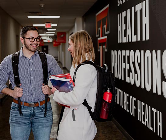 Two students with backpacks facing each other smiling