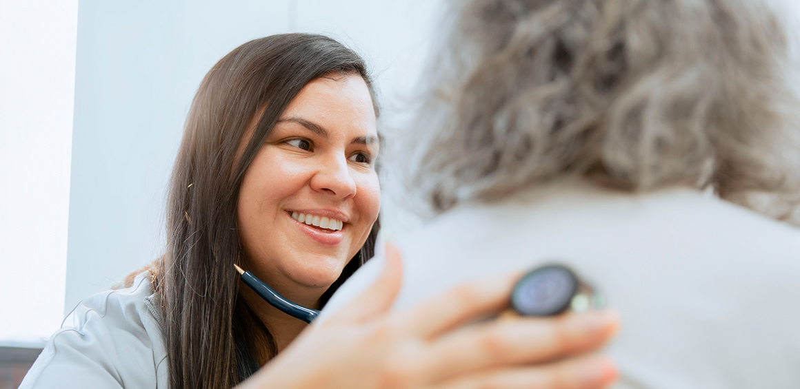 TTUHSC provider in a white lab coat holding a stethoscope to a patient on her back in a patient room