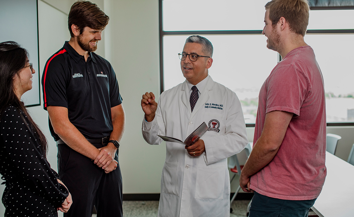 Three medical professionals in white coats are walking and talking together in a clinic hallway.