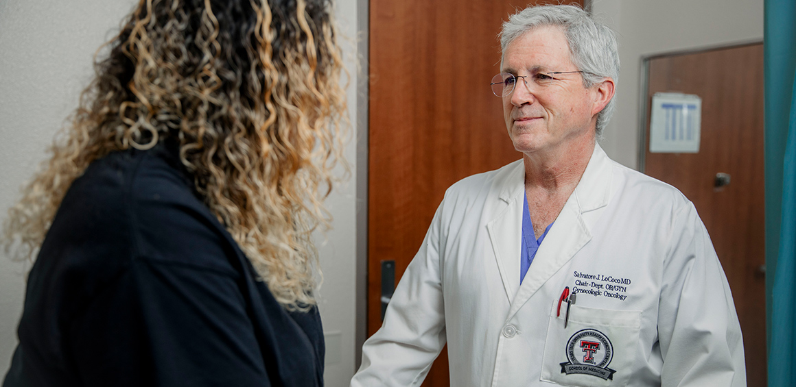 TTP provider in white lab coat smiling at a patient sitting on a patient's table in a clinic room