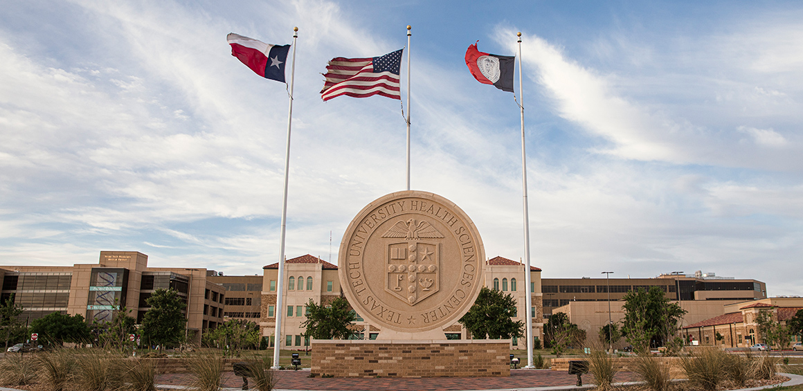 photo of Lubbock TTUHSC campus with seal and flagpoles on a sunny day