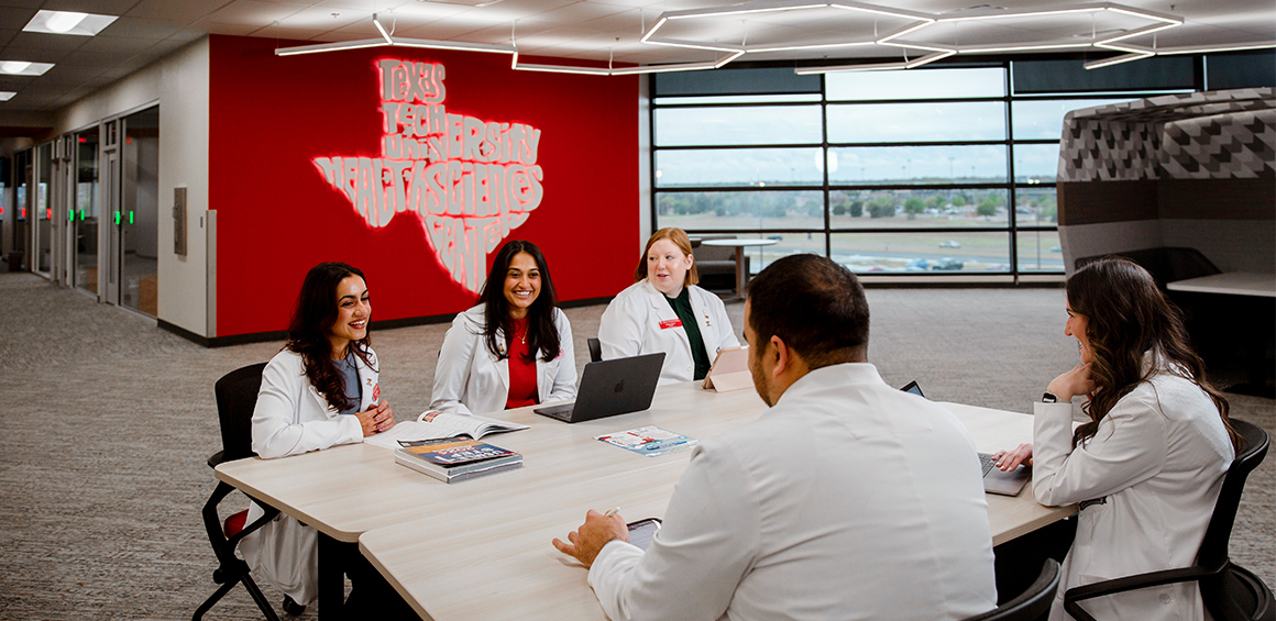 five students in white coats sitting around a table in the TTUHSC library smiling