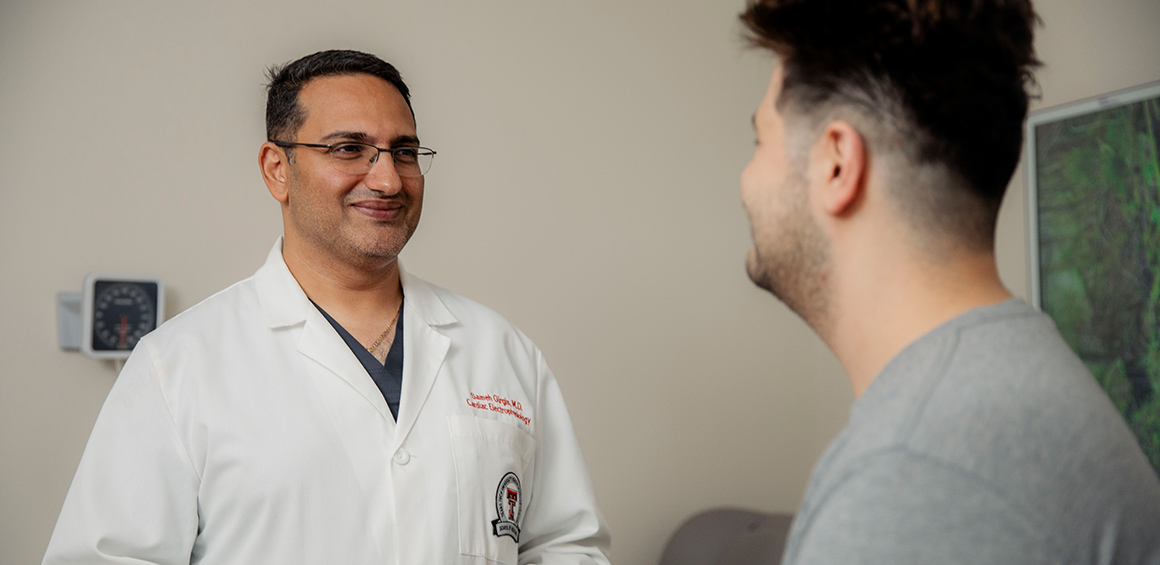 TTUHSC faculty member in white lab coat standing, smiling infront of patient sitting on a patient table in a grey tshirt