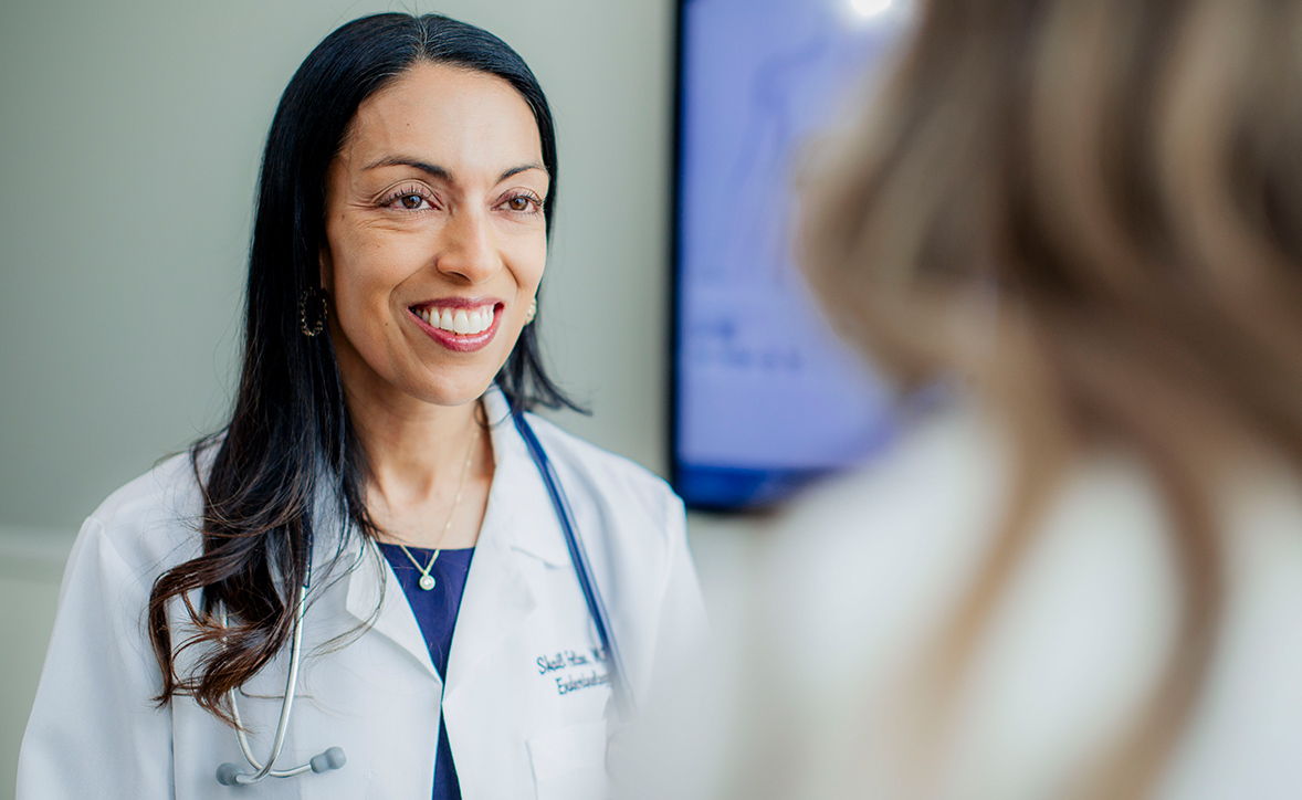 Smiling female endocrinologist in a white coat speaking with a patient during a clinic visit.