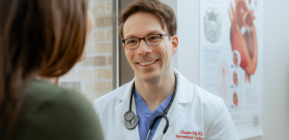 TTUHSC Alumni Dr. Sly standind with a pateint in a patient room smiling in a white lab coat