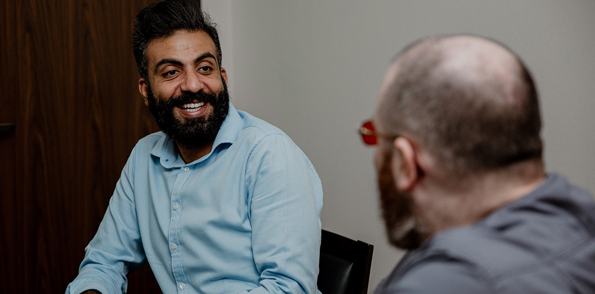 two gentlemen sitting in chairs facing each other smiling and conversing