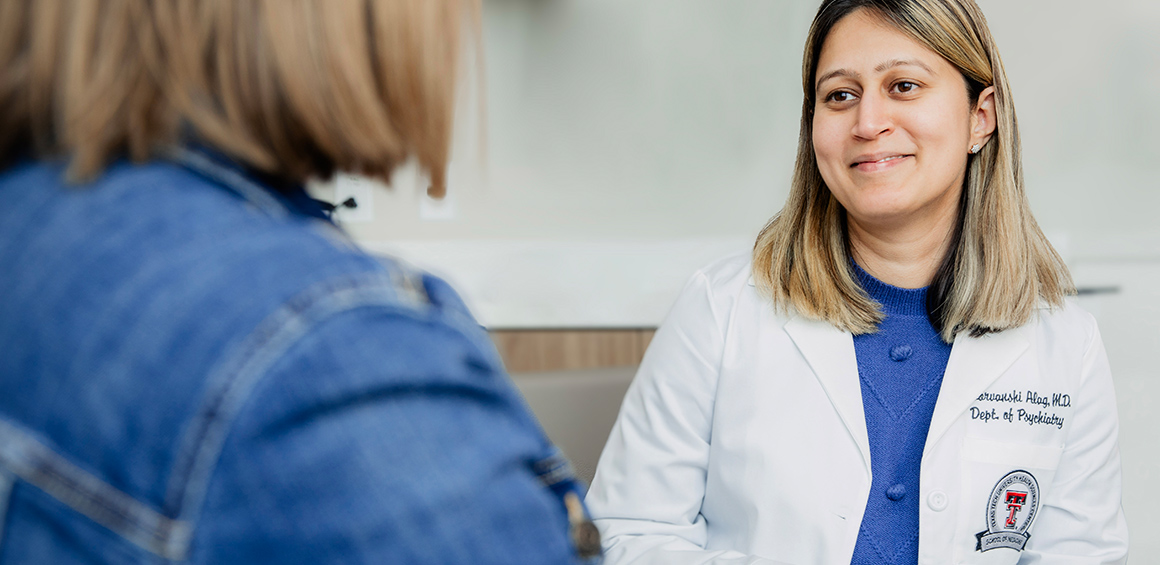 Texas Tech Physician sitting in a white coat smiling with a patient in a patient's room