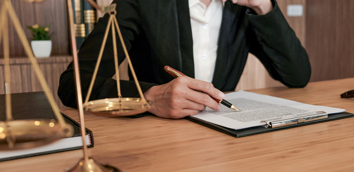 hands on a table holding a pen and papers on a clipboard with a gold scale figurine on the counter