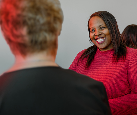 women in red sweater smiling at another woman in a black top facing away