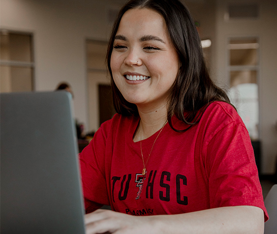 student in red shirt on a laptop smiling