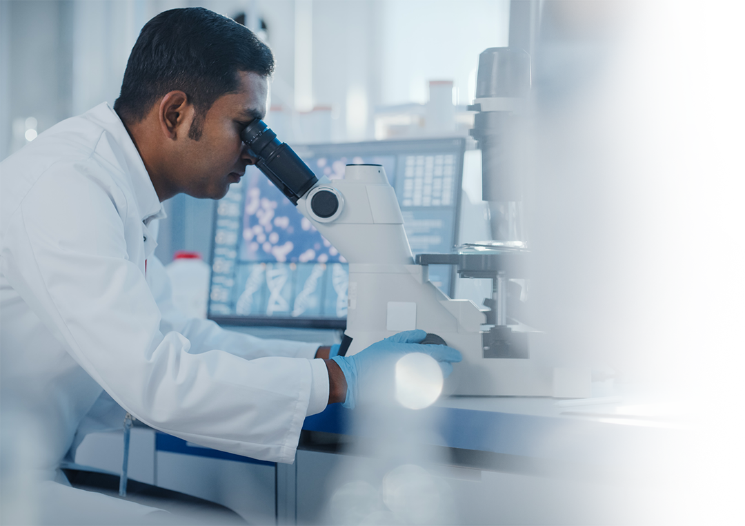 Student Worker in white coat and a lab setting looking through microscope