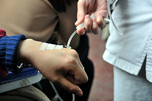 closeup of care provider's hand on IV line to patient's hand