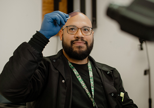 Lazaro Castillo in black scrubs holding up an object looking at it